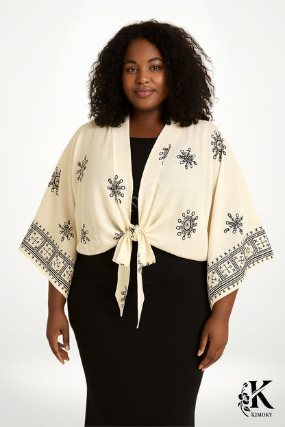 Femme souriante portant un kimono beige avec des motifs noirs, noué à la taille, devant un fond blanc