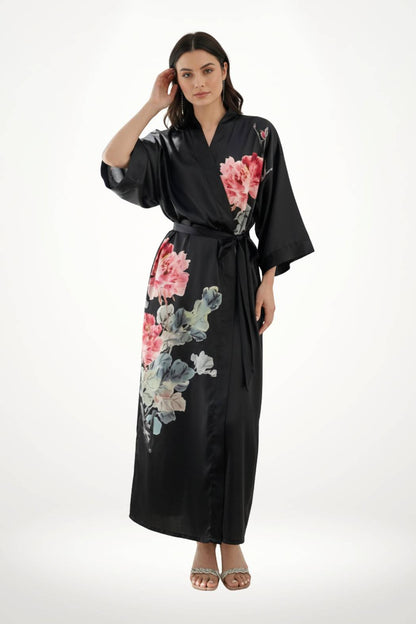 Femme en kimono noir en satin, décoré de fleurs roses, se tenant debout avec une main dans les cheveux