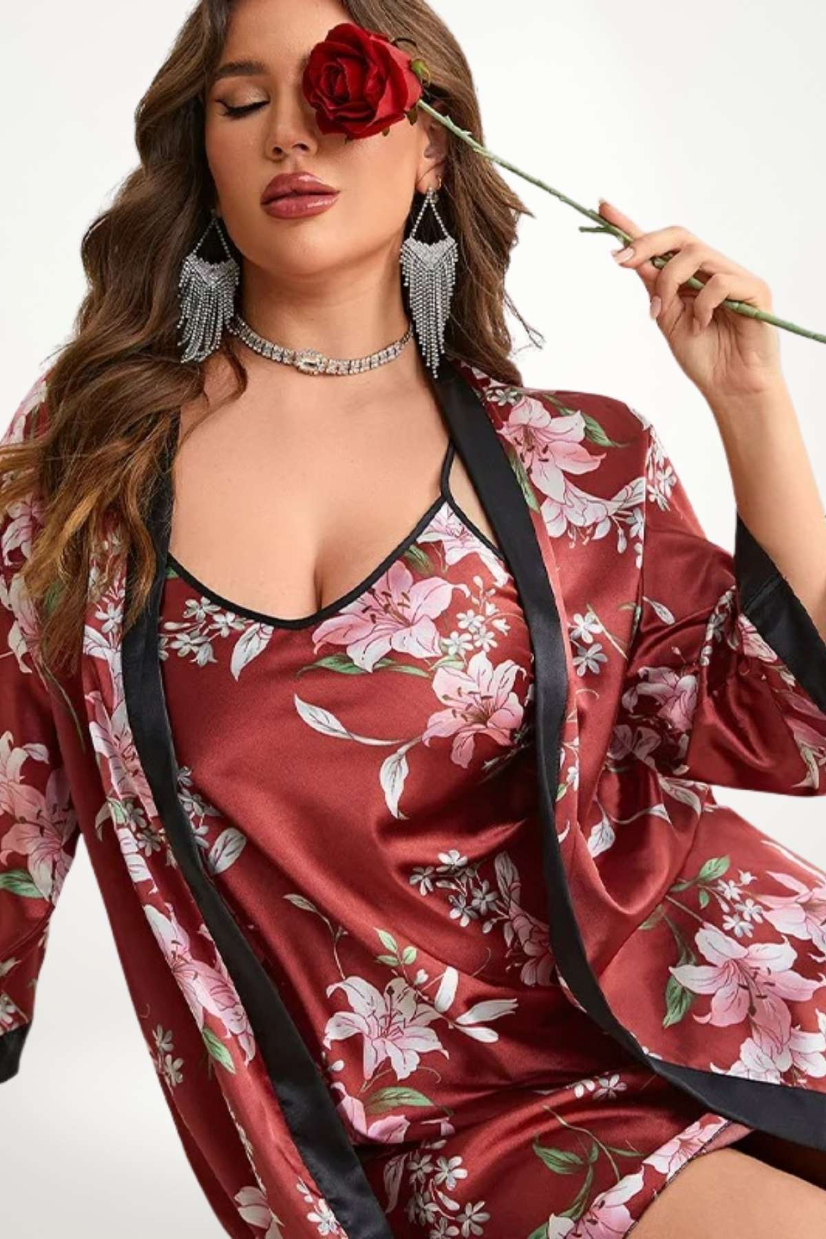 Femme portant un kimono en satin rouge à fleurs, posant avec une rose et des bijoux scintillants