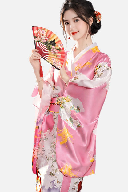 Femme souriante en kimono rose satiné avec motifs floraux, tenant un éventail décoratif aux couleurs vives