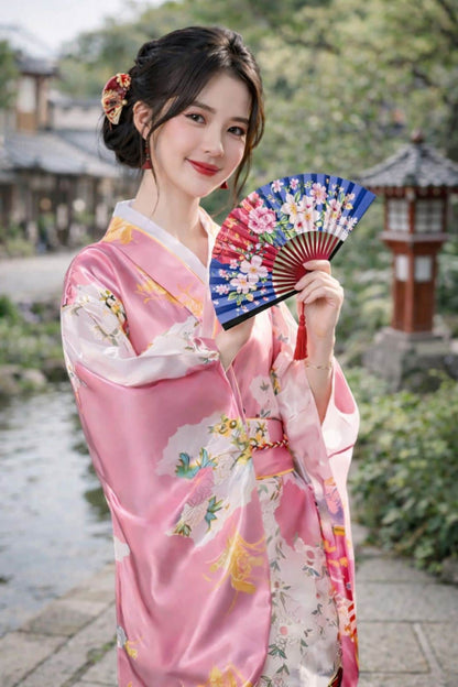 Femme en kimono rose avec motifs floraux, tenant un éventail coloré, dans un décor naturel et traditionnel japonais