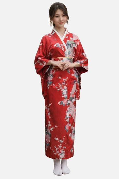 Femme en kimono rouge orné de fleurs, avec ceinture dorée, posant élégamment sur fond neutre