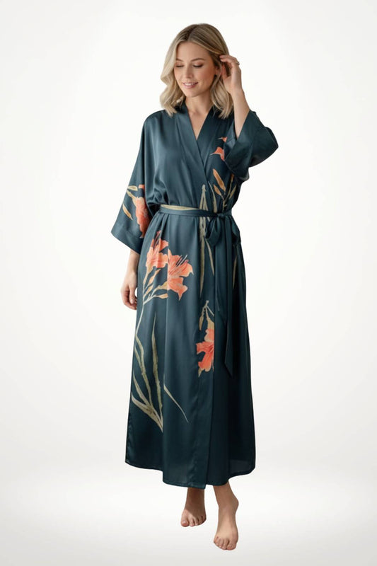 Femme souriante portant un kimono long en satin bleu-vert avec des motifs floraux orange, dans un décor minimaliste