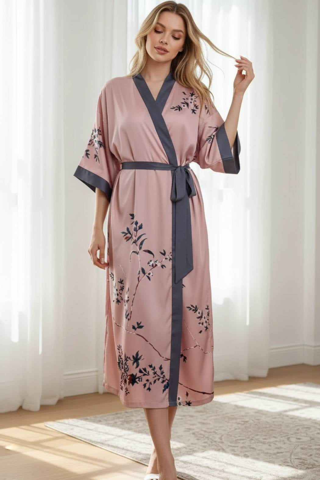 Kimono en satin rose avec motifs floraux noirs, ceinturé à la taille, dans un intérieur lumineux et élégant