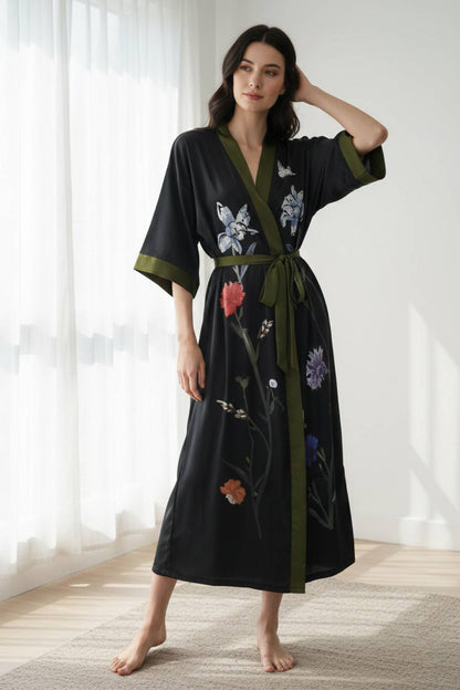 Kimono noir élégant avec des motifs floraux colorés et une ceinture verte, porté par une femme debout dans un intérieur