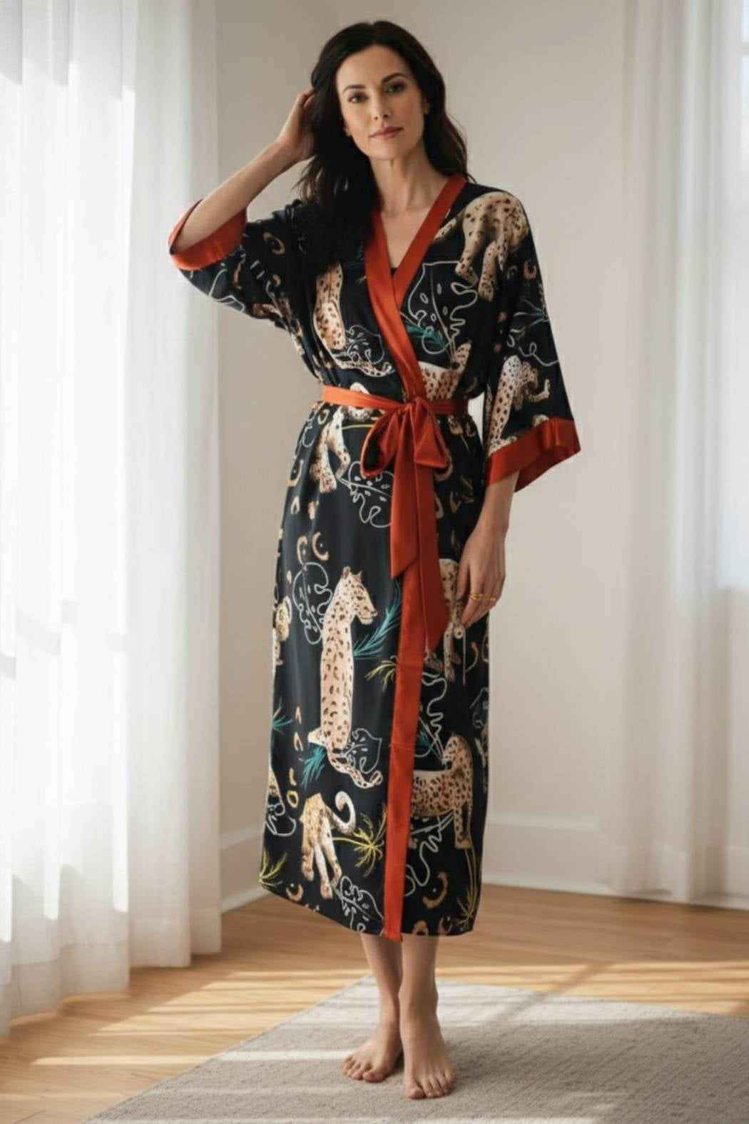 Une femme porte un kimono noir à motifs félins avec des détails en satin orange, dans un décor lumineux et