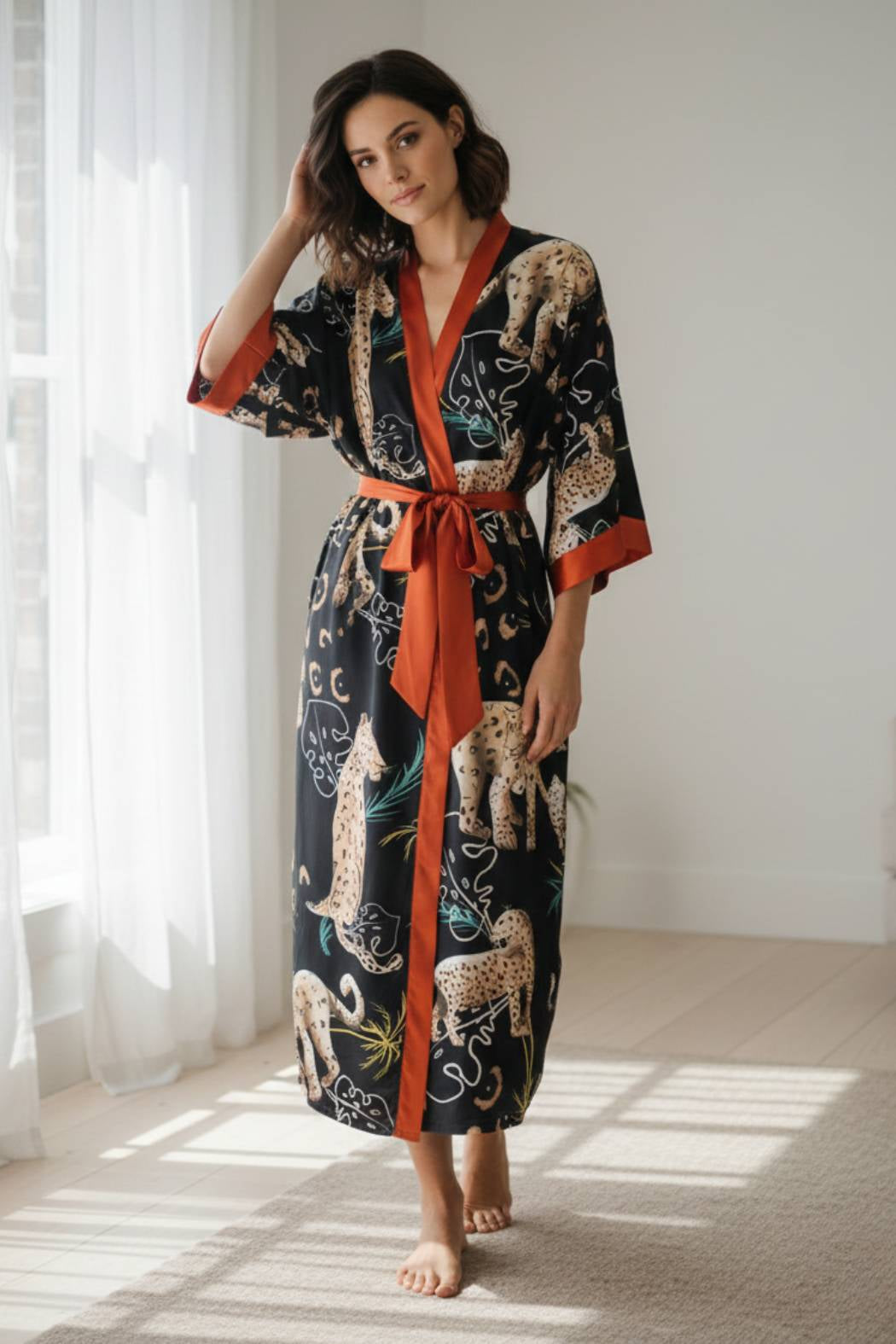 Femme portant un kimono noir à motifs félins avec des détails orange, dans un décor lumineux et minimaliste