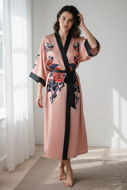 Femme portant un kimono long rose avec des motifs floraux, ceinturé de noir, dans un décor lumineux et moderne