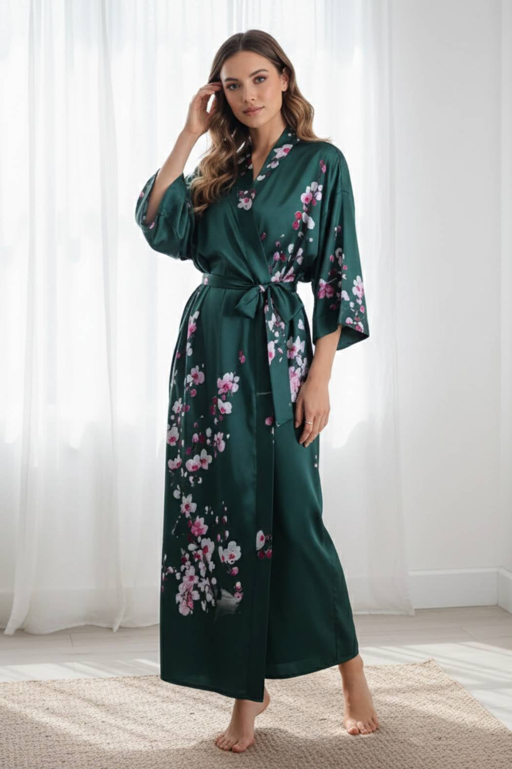 Kimono long en satin vert émeraude avec motifs floraux roses, porté par une femme dans un décor lumineux