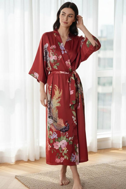 Femme en kimono long satiné rouge avec motifs floraux, posant dans un intérieur lumineux et élégant