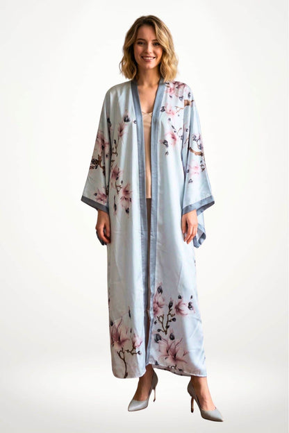 Femme souriante portant un kimono long bleu avec des motifs floraux roses sur fond clair