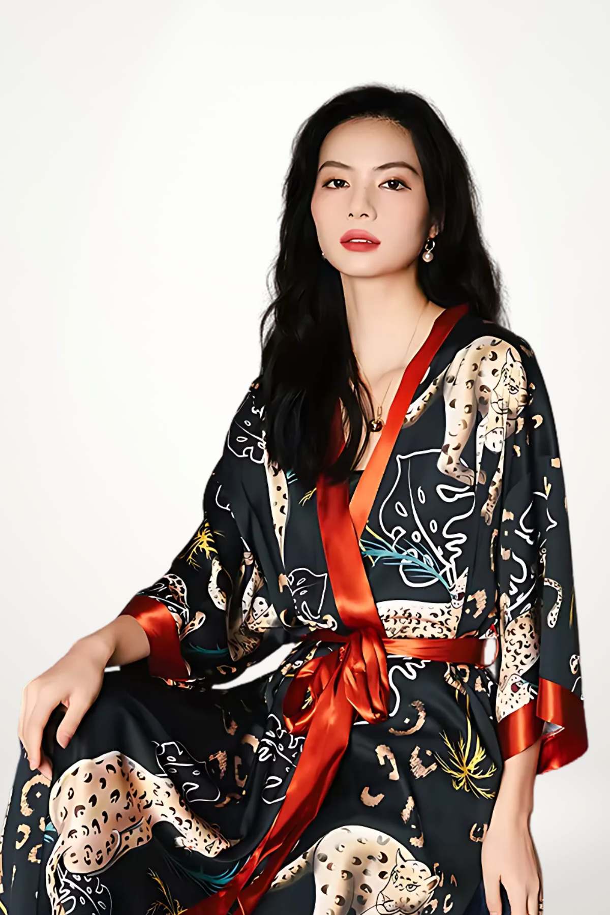 Femme portant un kimono noir avec motifs félins, ceinture satinée rouge, fond neutre et posture élégante