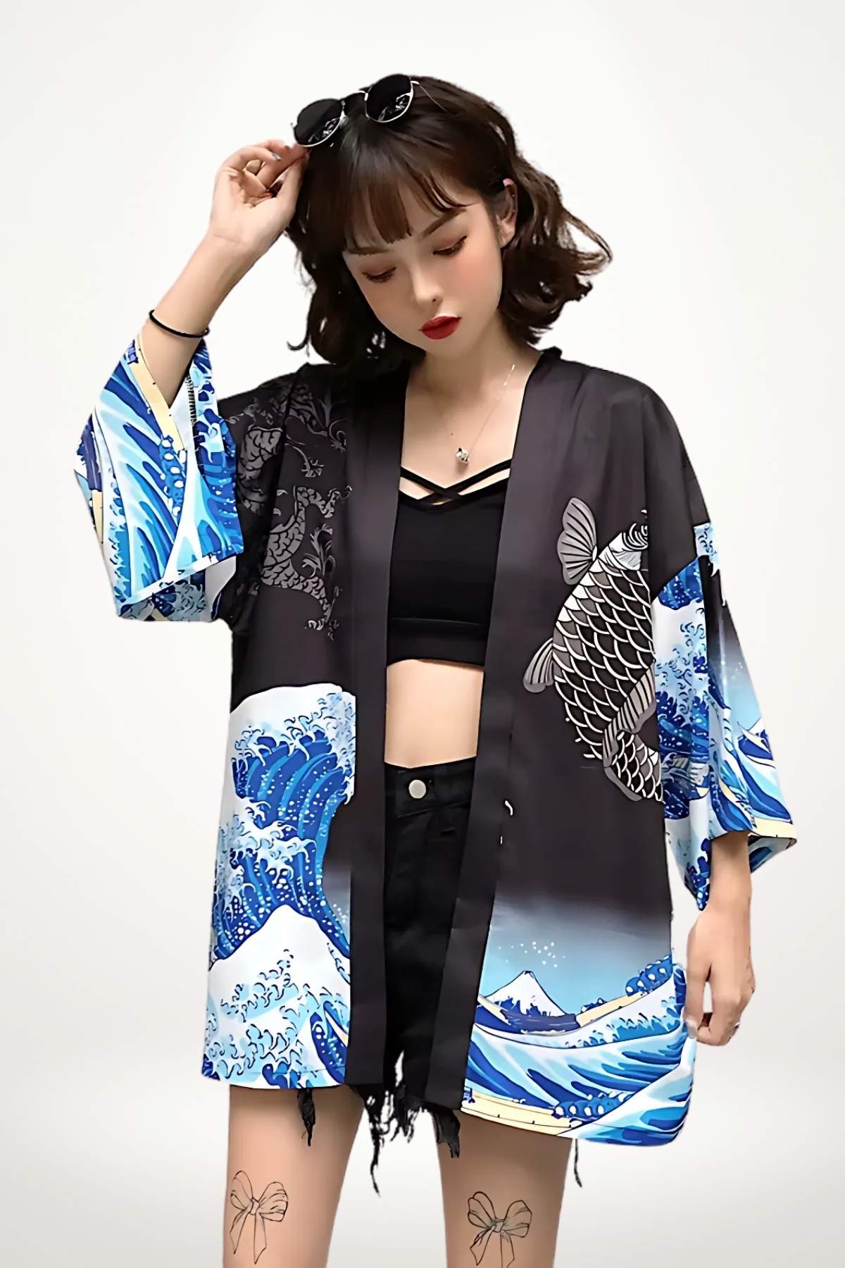 Femme portant un kimono noir avec motifs de vagues bleues, associé à un top noir et un short en denim