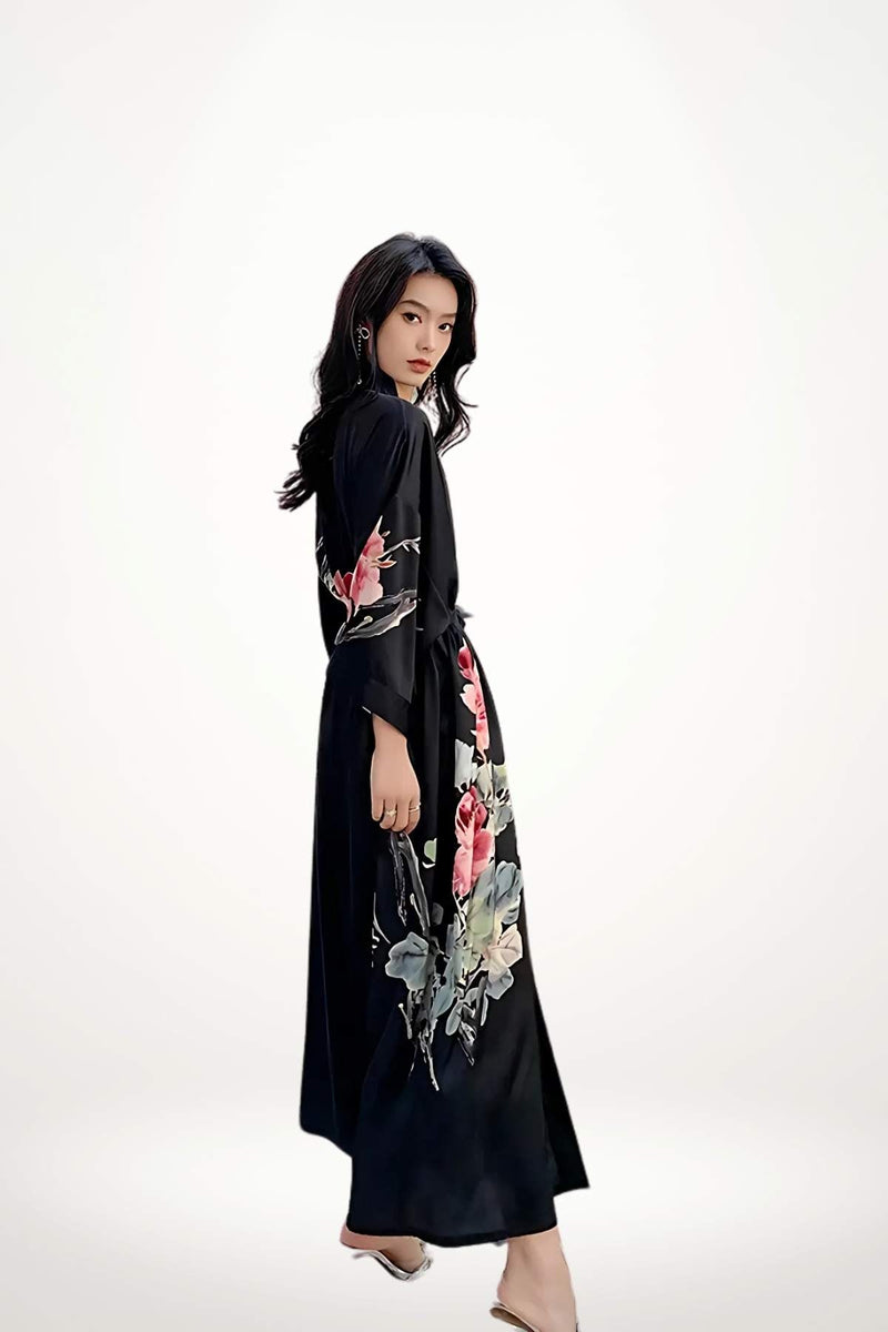 Femme en kimono noir en satin, avec des motifs floraux colorés sur les manches, se tenant de profil
