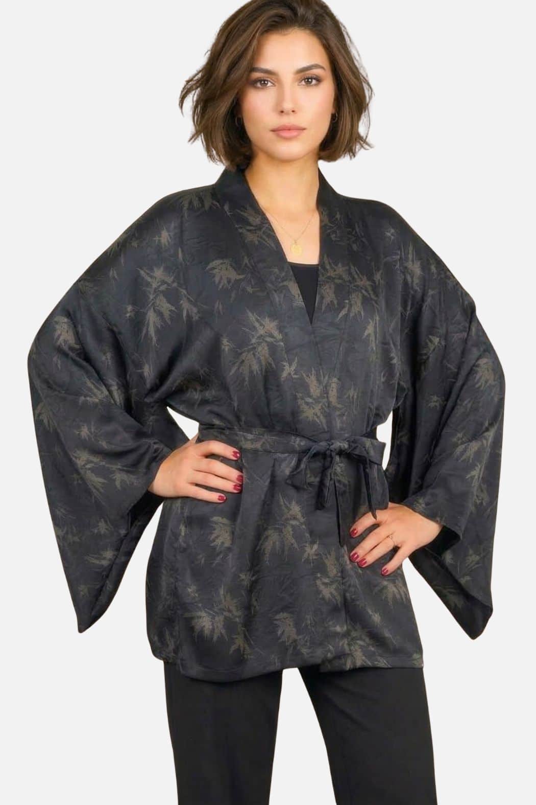 Femme portant un kimono noir avec des motifs de feuilles, dans une posture élégante et décontractée