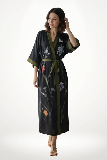 Femme portant un kimono noir élégant avec des motifs floraux colorés et une ceinture verte, sur fond neutre