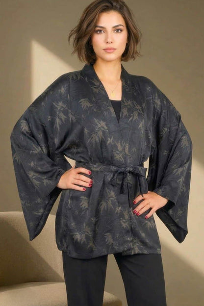 Femme portant un kimono noir avec des motifs de feuilles, dans un décor élégant et lumineux