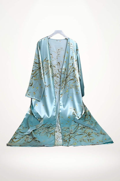 Kimono léger en satin bleu orné de motifs floraux dorés, suspendu sur un cintre dans un décor minimaliste