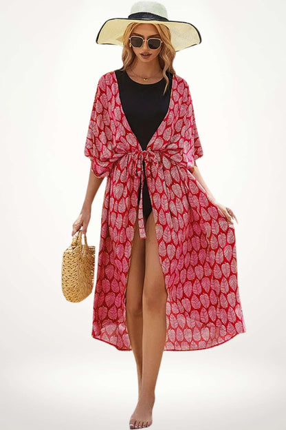 Femme portant un kimono rouge à motifs feuilles, avec un chapeau large et un sac en osier, sur une plage