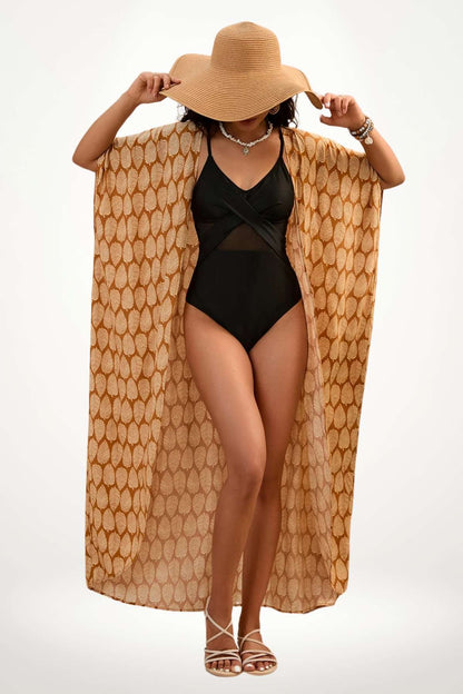 Femme portant un kimono à motifs feuilles dorées sur un maillot noir, chapeau en paille et sandales blanches