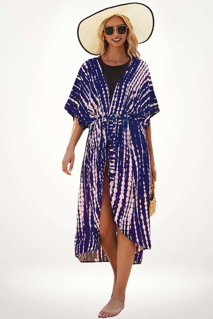 Femme portant un kimono bleu marine à motifs roses, avec un chapeau large, sur une plage ensoleillée