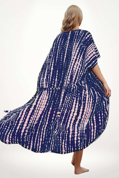 Femme en kimono bleu marine à motifs roses, se tenant sur la plage, vêtue d'un tissu léger et fluide