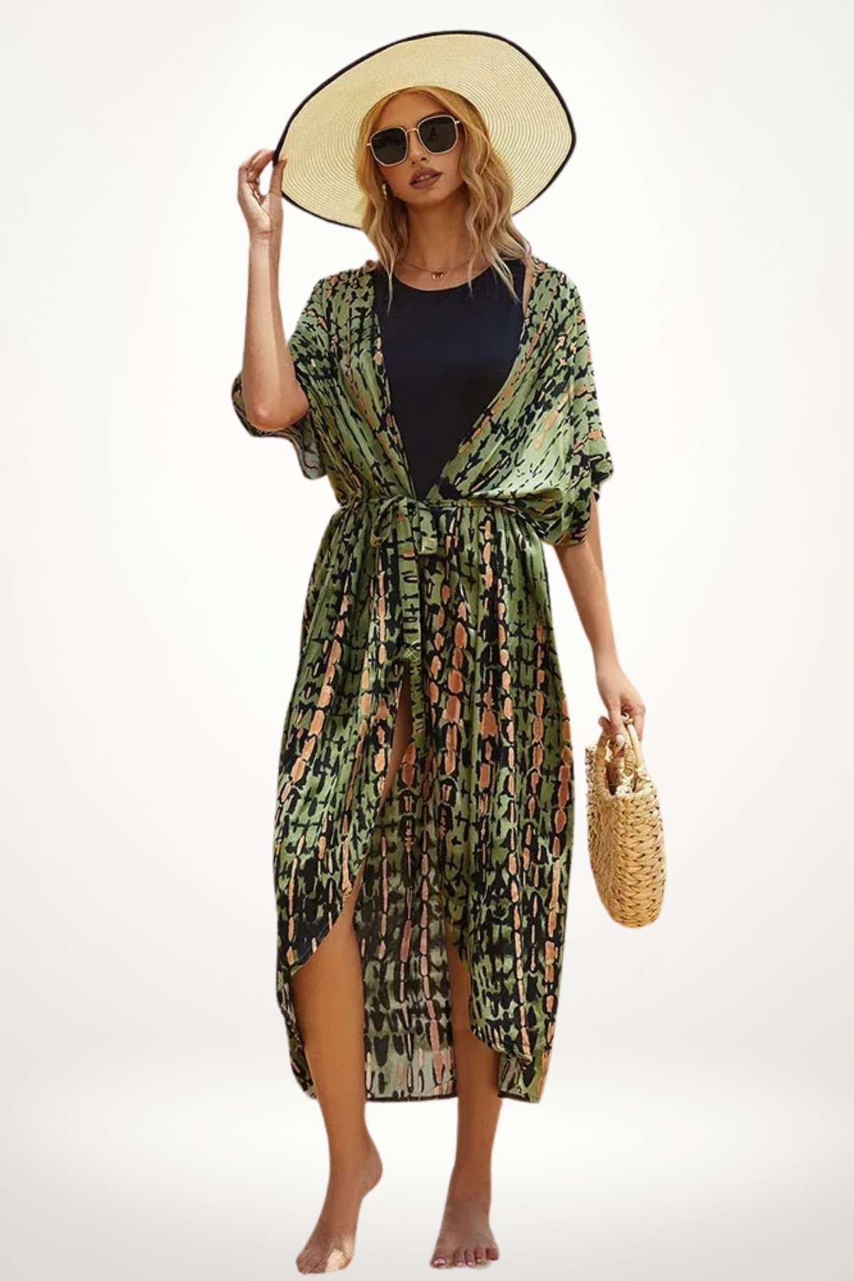 Femme en kimono vert à motifs, portant un chapeau large, posant sur une plage avec un sac en osier