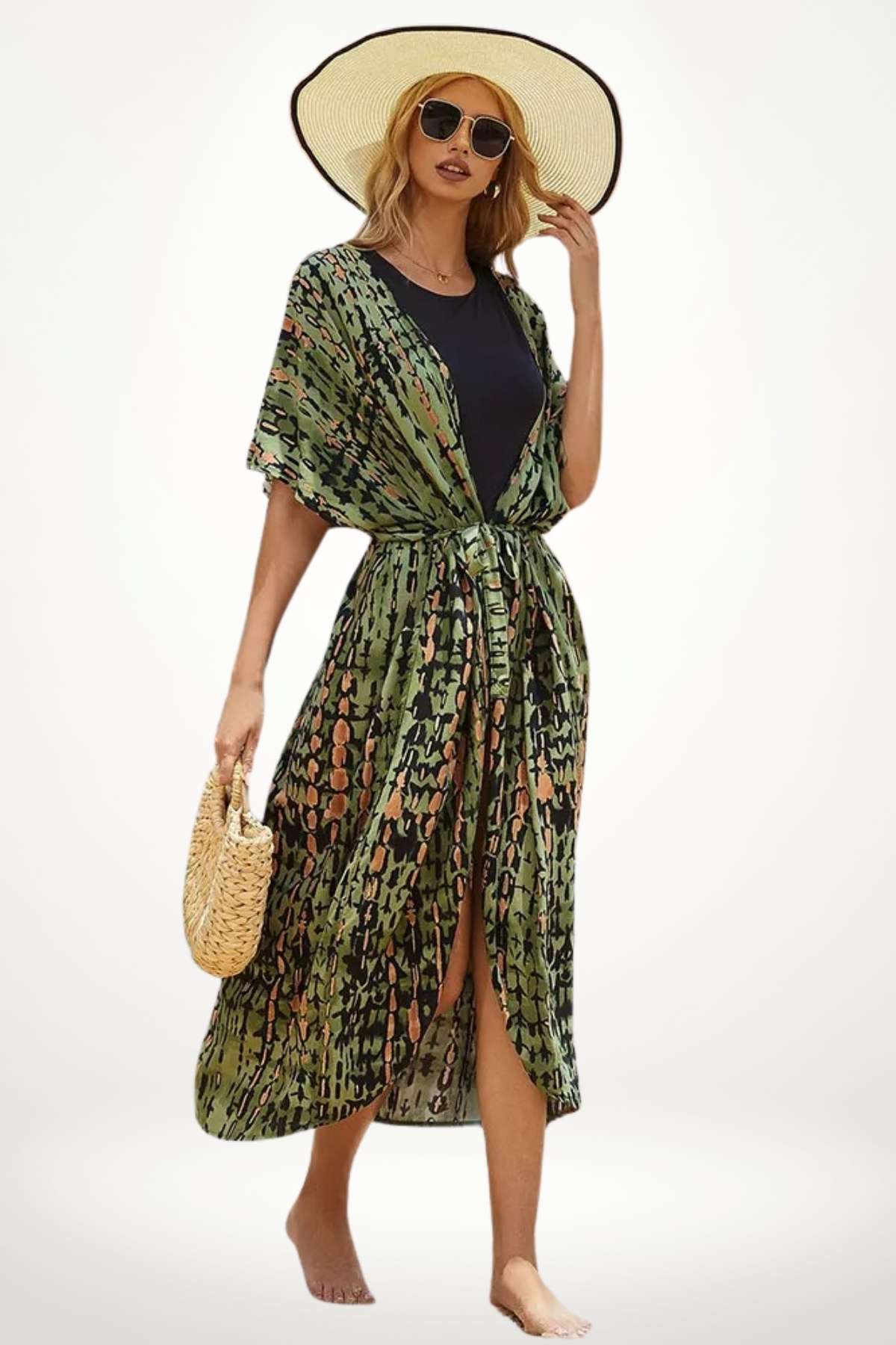 Femme en kimono vert à motifs, portant un chapeau large, se tenant sur une plage avec un sac en osier