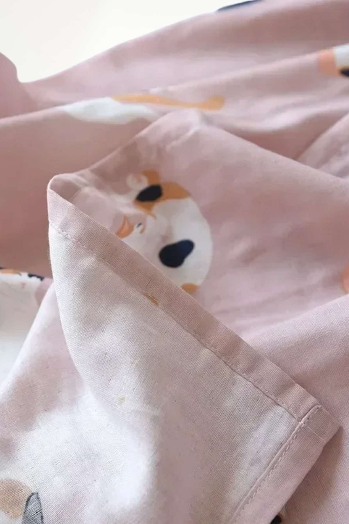 Tissu en coton rose avec motifs de visages stylisés, plié avec des contours soignés et une texture douce