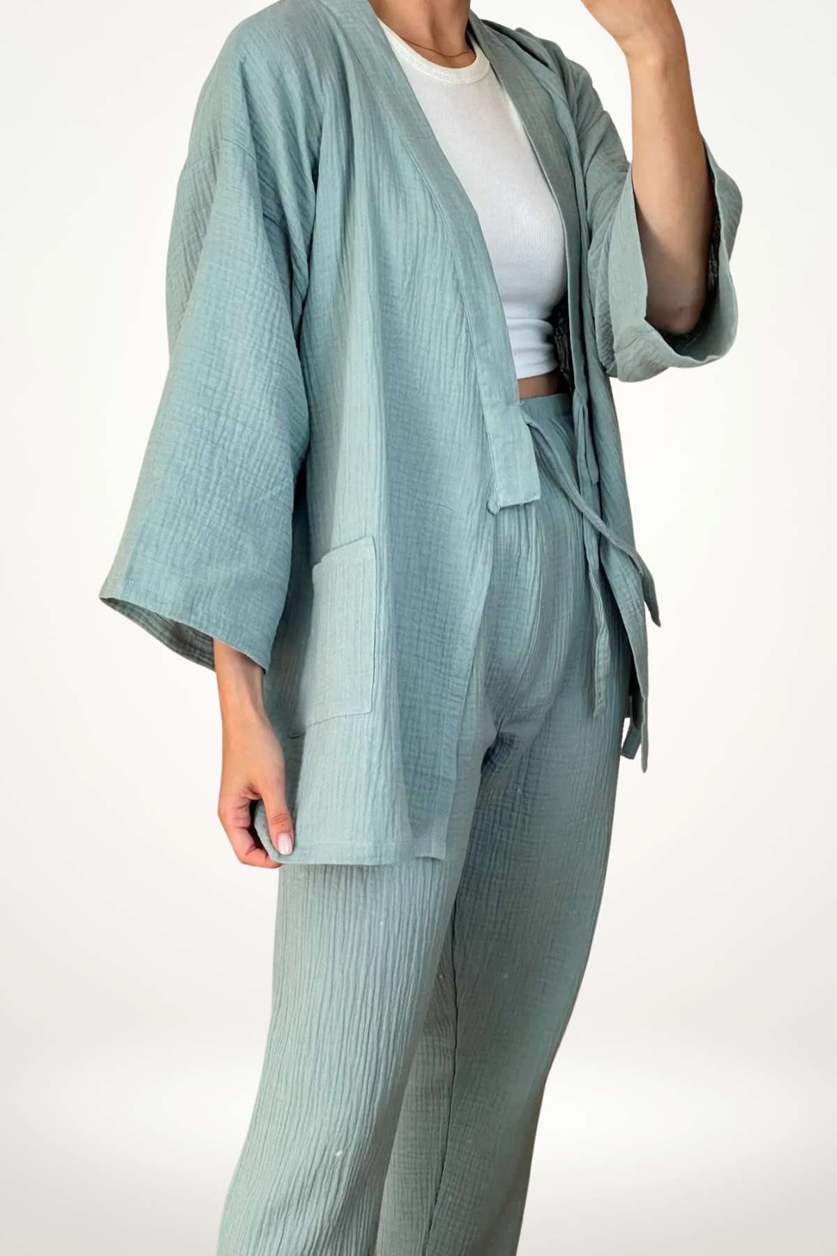 Femme portant un kimono vert en tissu léger avec un pantalon assorti, dans un décor minimaliste
