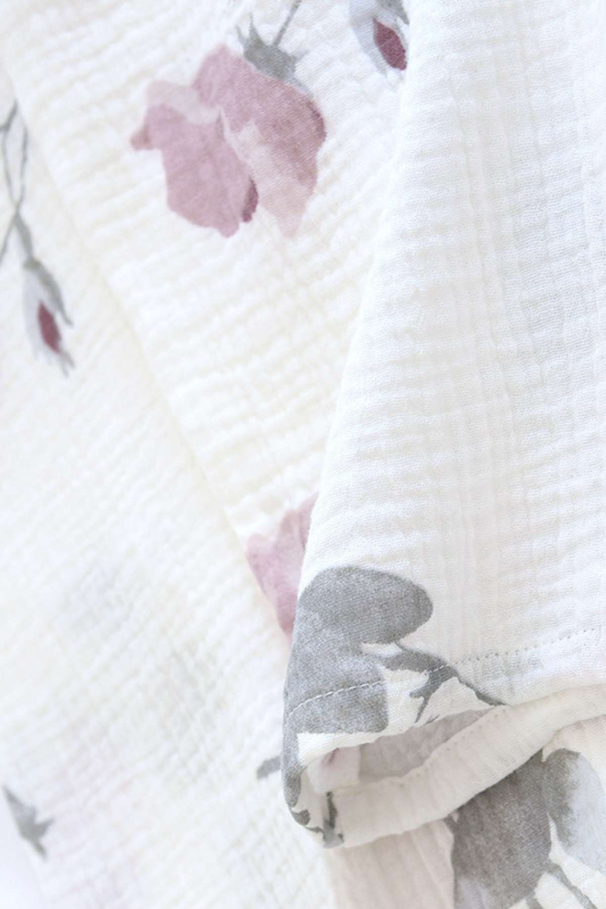 Tissu léger blanc avec motifs floraux roses et gris, offrant une texture douce et confortable