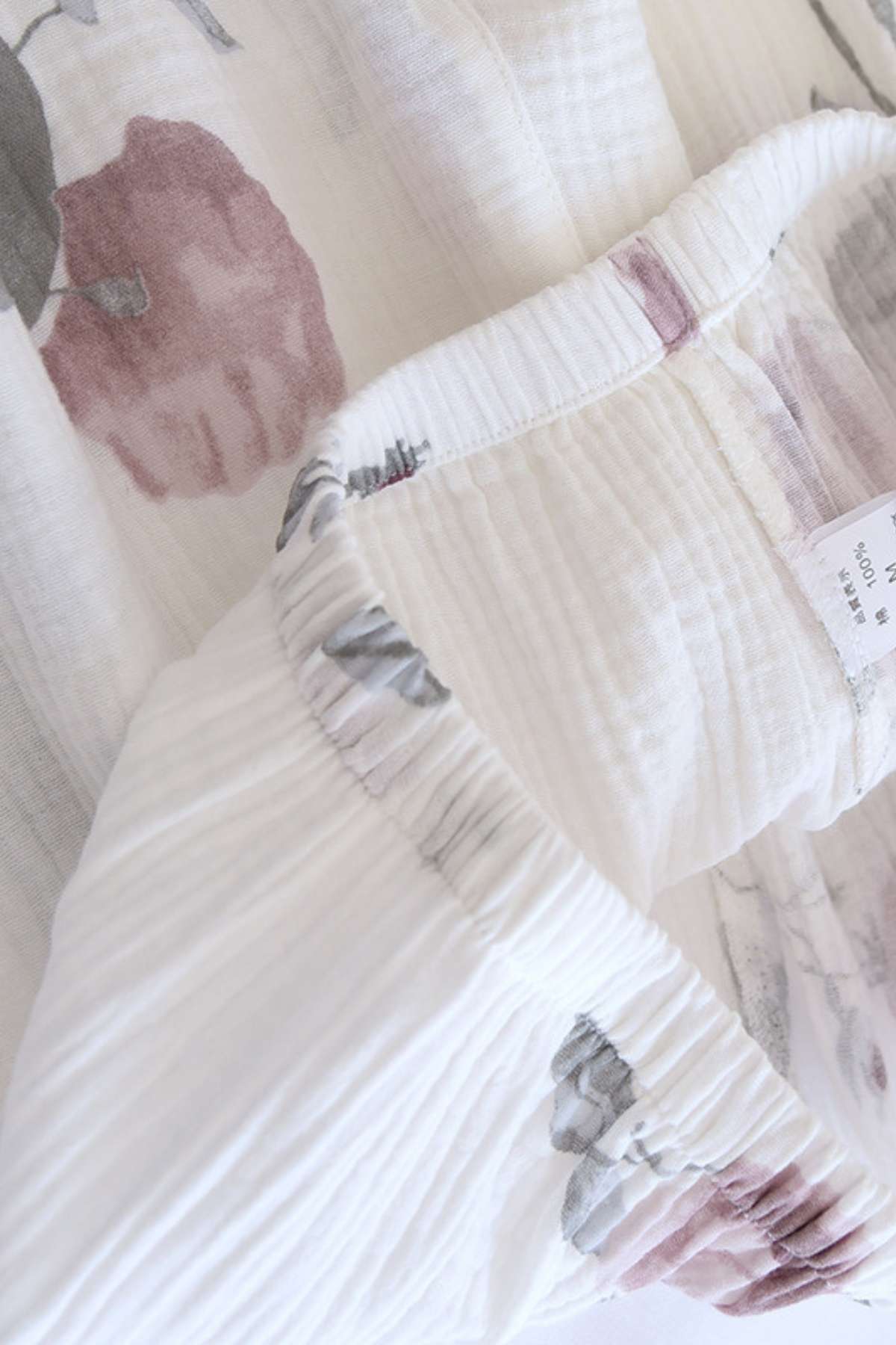 Tissu léger en coton avec motifs floraux roses et gris sur fond blanc, offrant confort et douceur