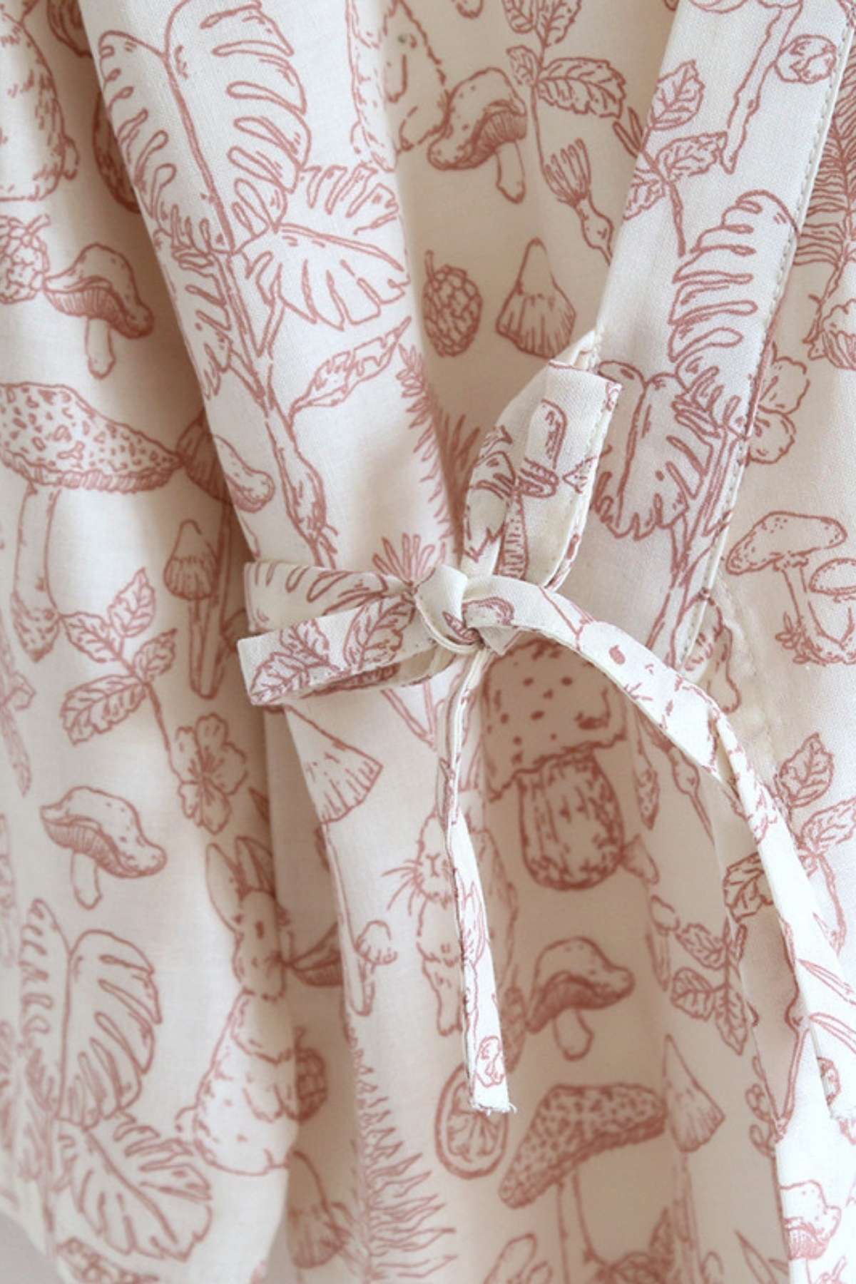 Détail d'un kimono en coton doux avec motifs floraux et animaux dans des teintes rose pâle sur fond crème
