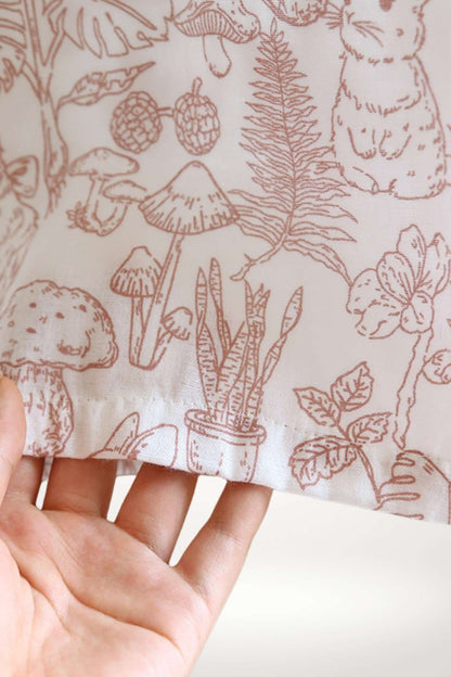 Main tenant délicatement un tissu en coton avec un motif floral et des champignons dans des teintes rose pâle