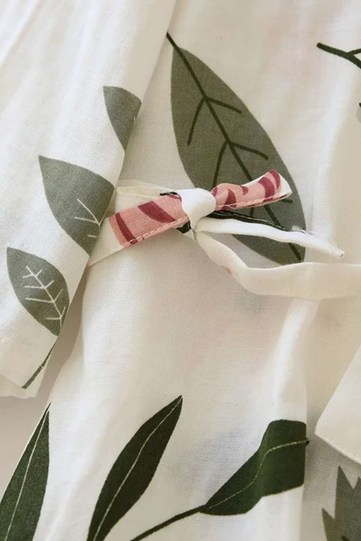 Tissu léger avec motifs de feuilles vertes sur fond blanc, noué avec un ruban à rayures roses
