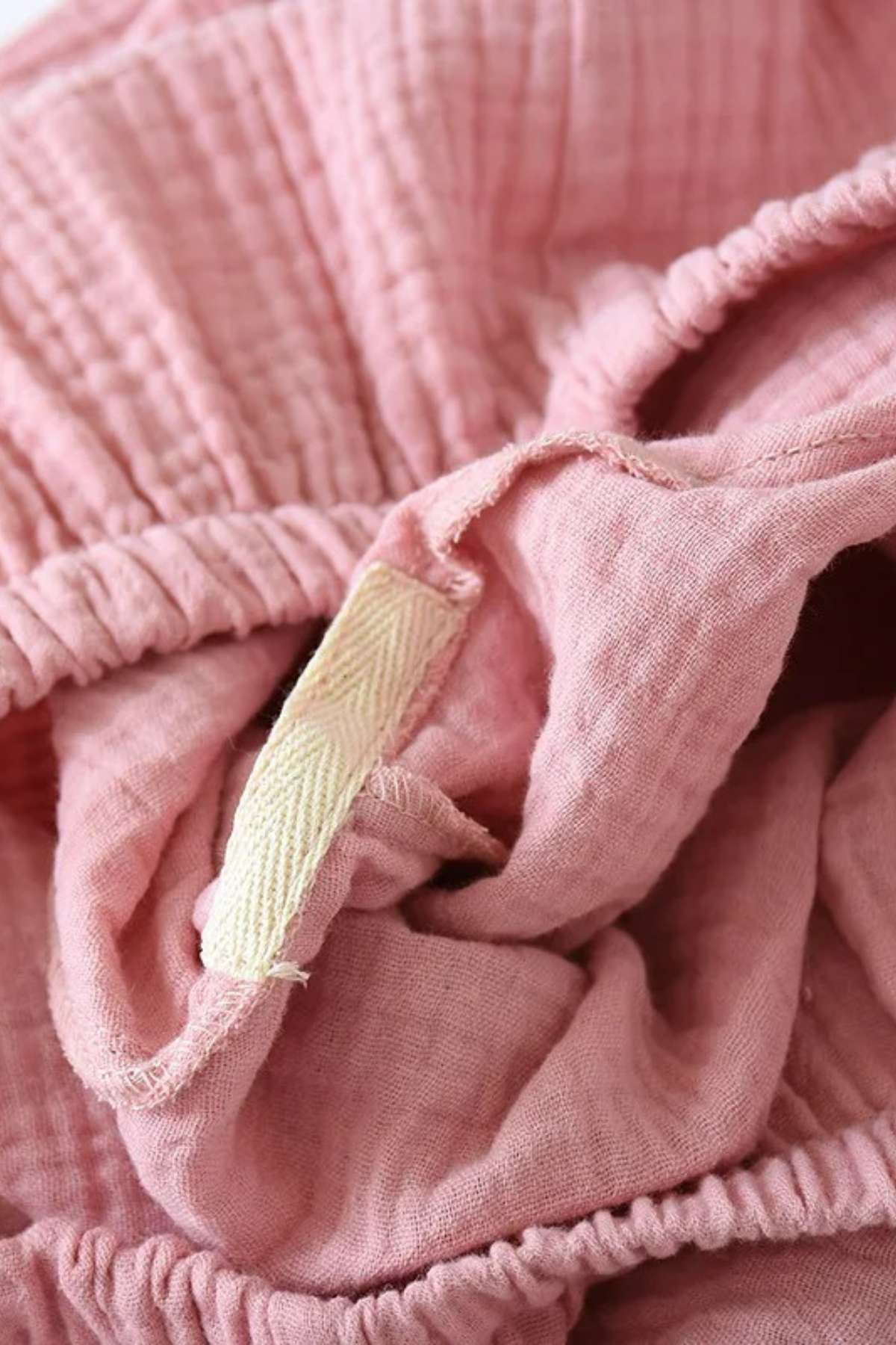 Tissu rose doux et léger, avec des plis et une étiquette en tissu beige, évoquant un style de pyjama confortable