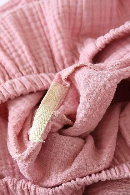 Tissu rose doux et léger, avec des plis et une étiquette en tissu beige, évoquant un style de pyjama confortable