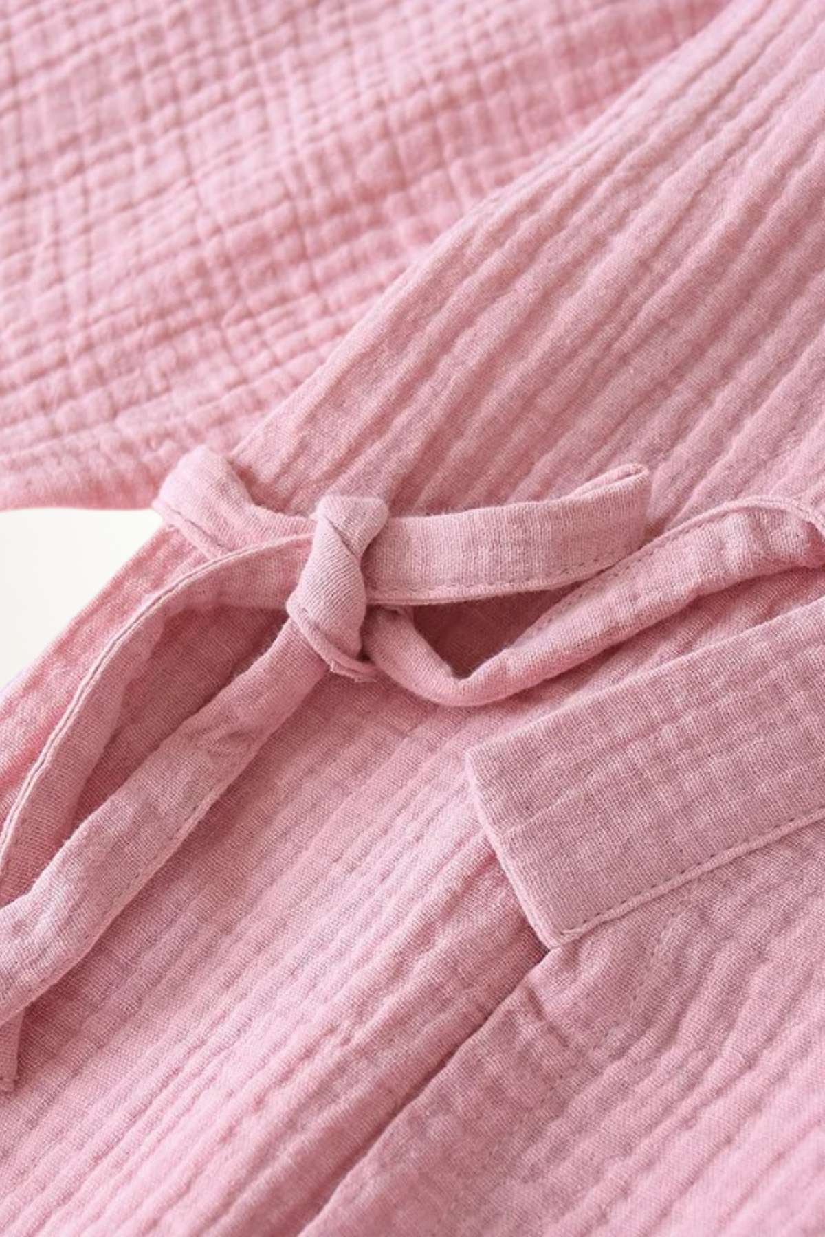 Détail d'un kimono rose en tissu léger, avec un motif texturé et une ceinture nouée sur le devant