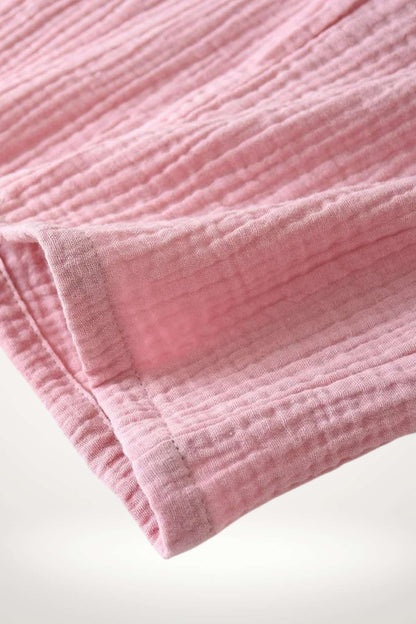 Tissu de kimono en coton rose, avec une texture gaufrée et des bordures délicates, reposant sur un fond neutre