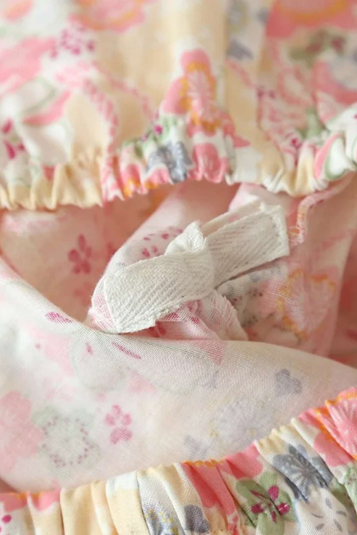 Tissu léger aux motifs floraux roses et jaunes, avec des fronces et un lien en tissu blanc