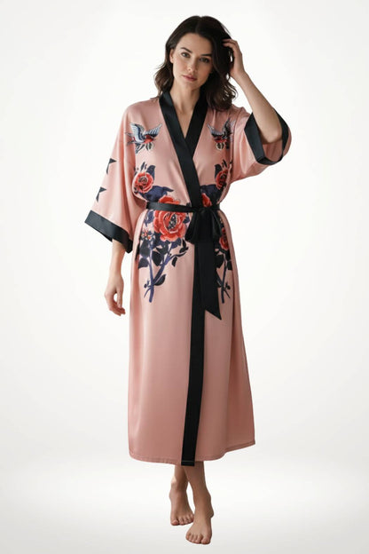 Kimono long en satin rose avec motifs floraux, ceinture noire, porté par une femme debout sur un fond blanc