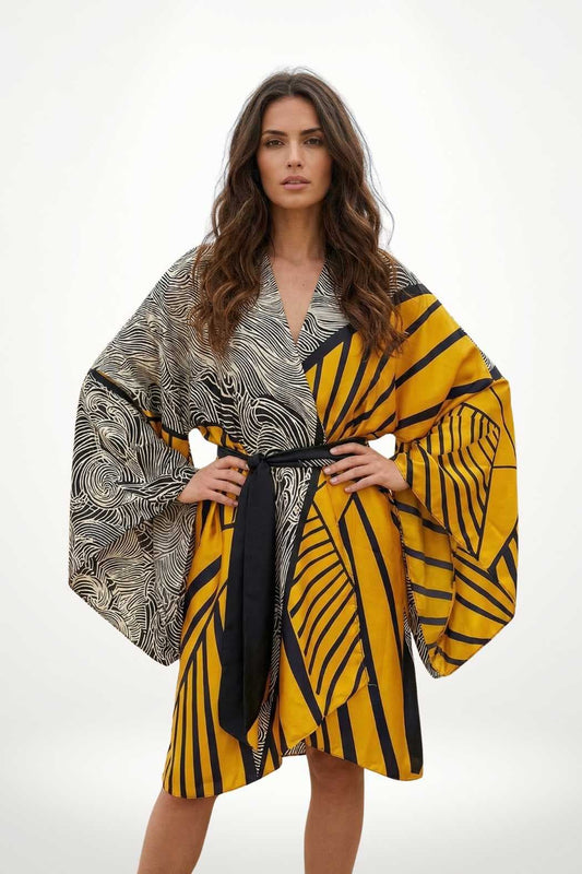 Femme portant un kimono en satin noir et jaune avec des motifs géométriques, pose confiante sur fond neutre