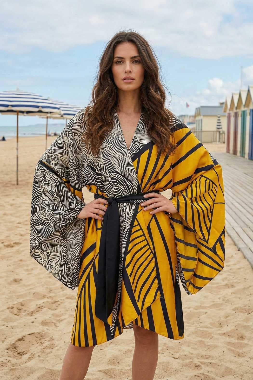 Femme portant un kimono en satin aux motifs noirs et jaunes, sur une plage avec des cabines colorées en arrière-plan