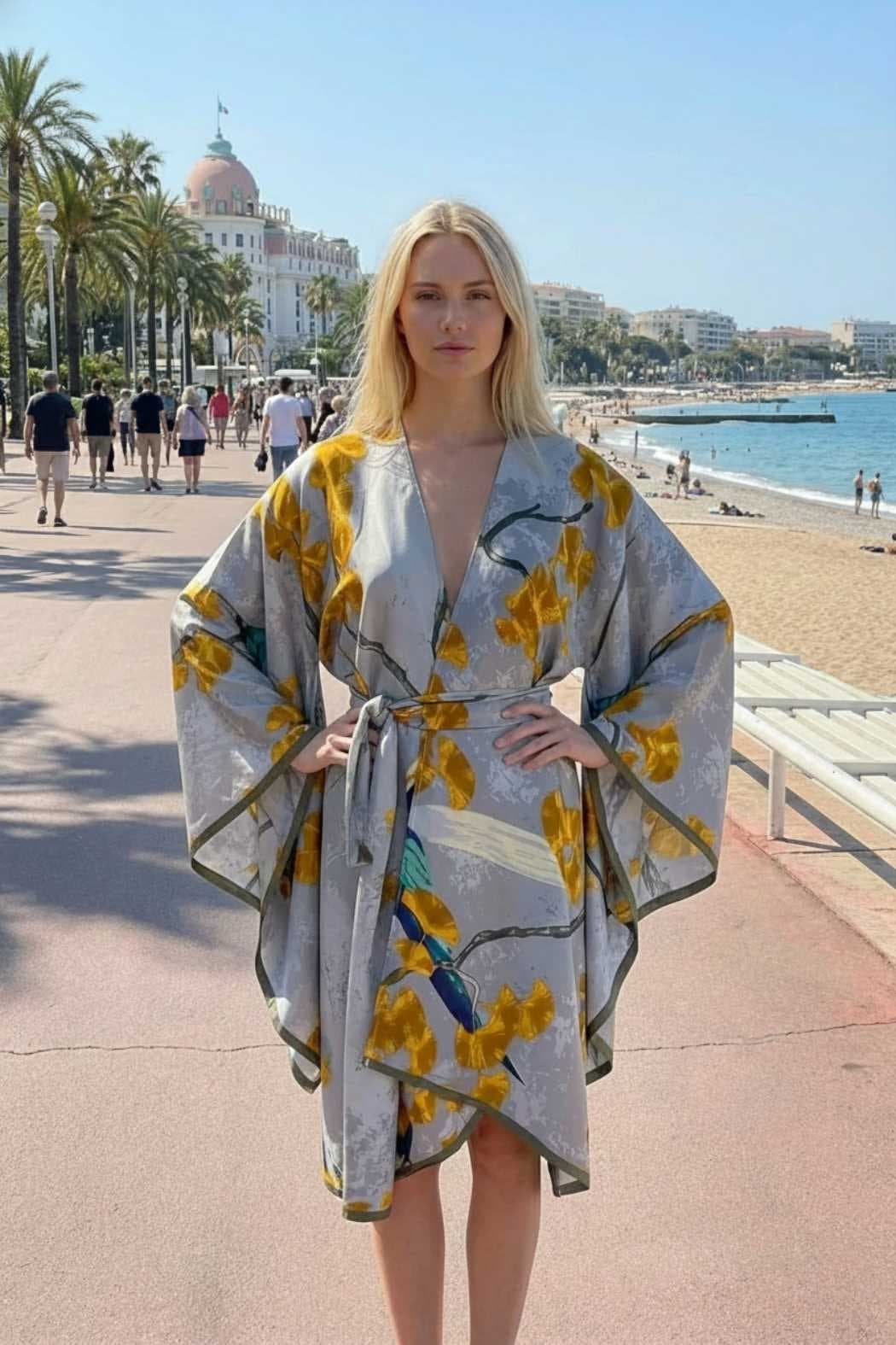 Femme portant un kimono gris avec des motifs floraux jaunes, sur un chemin en bord de mer ensoleillé