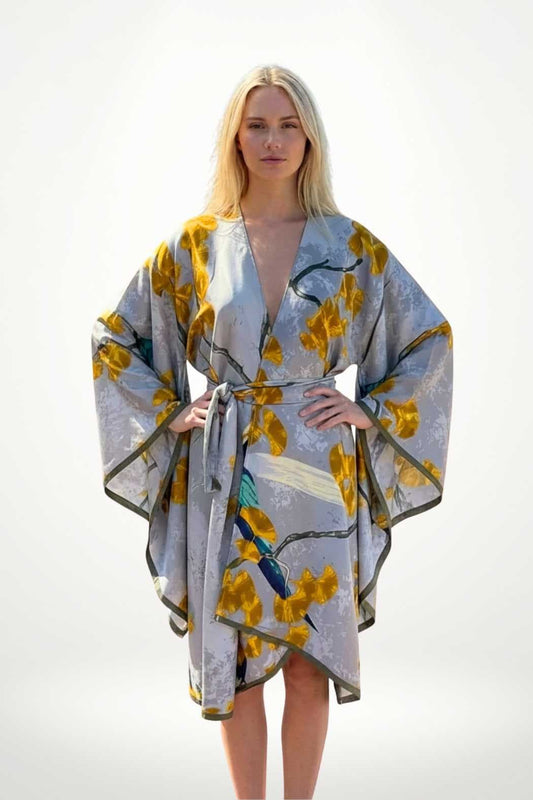 Robe kimono chic grise ornée de motifs floraux jaunes, portée par une femme aux cheveux blonds, dans un décor minimaliste