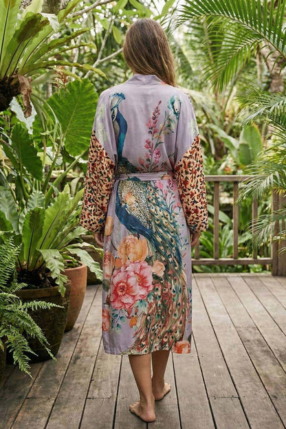 Femme de dos portant un kimono en satin violet avec motifs de paons et fleurs, dans un jardin tropical