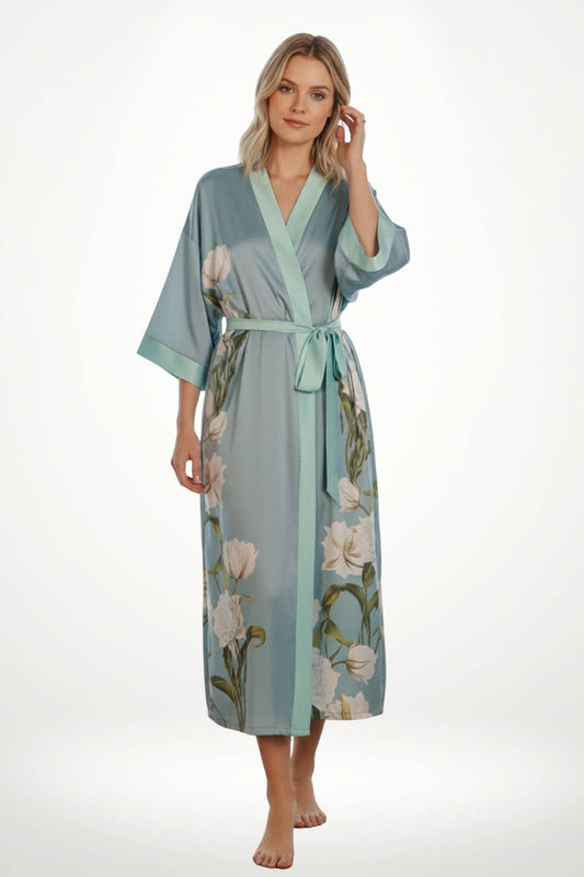 Kimono long en satin bleu clair avec des motifs floraux, ceinturé, porté par une femme souriante dans un décor neutre