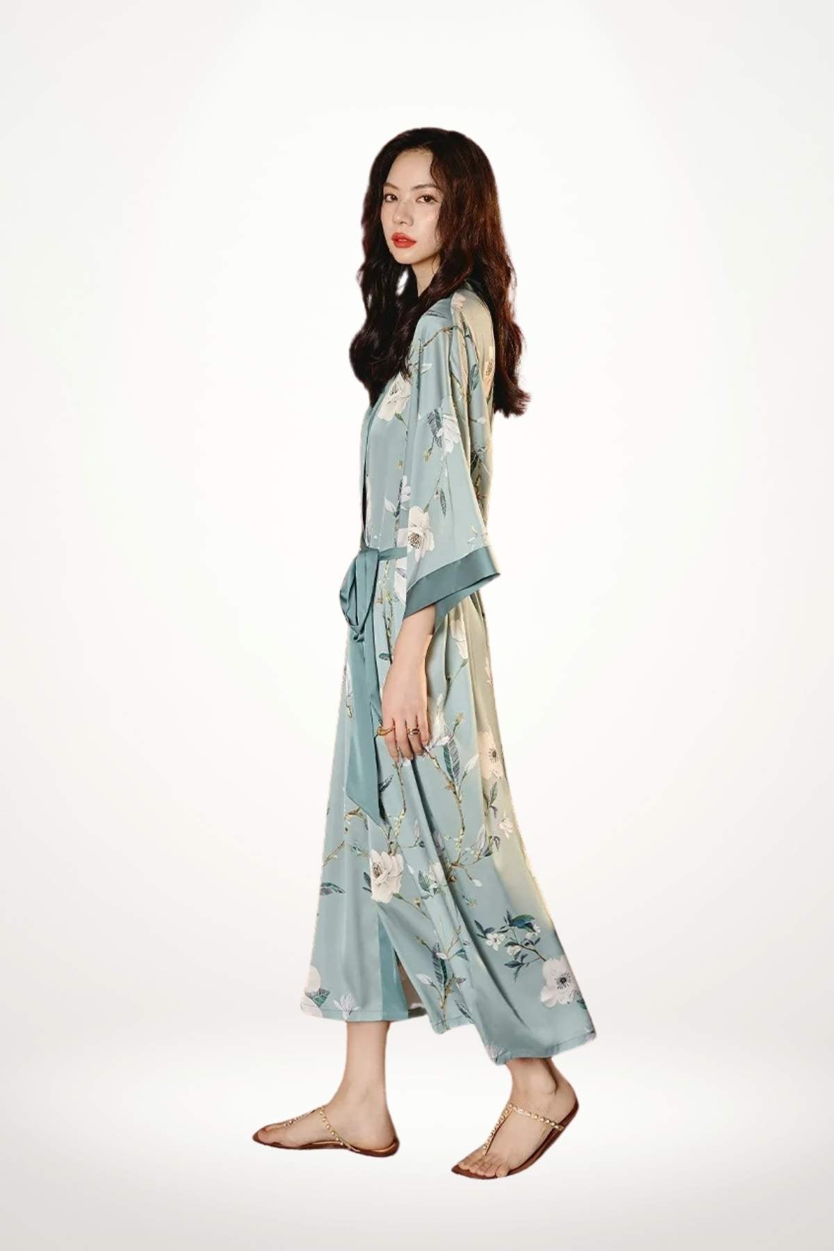 Femme en kimono léger bleu avec motifs floraux, posant sur fond blanc, cheveux longs et ondulés