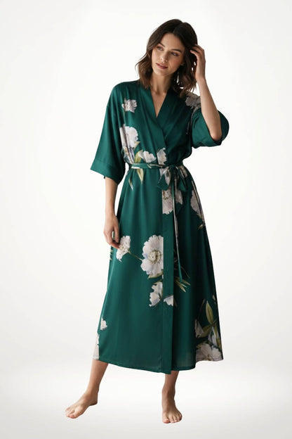Kimono vert avec des motifs floraux blancs, tissu léger, porté par une femme debout, décor minimaliste