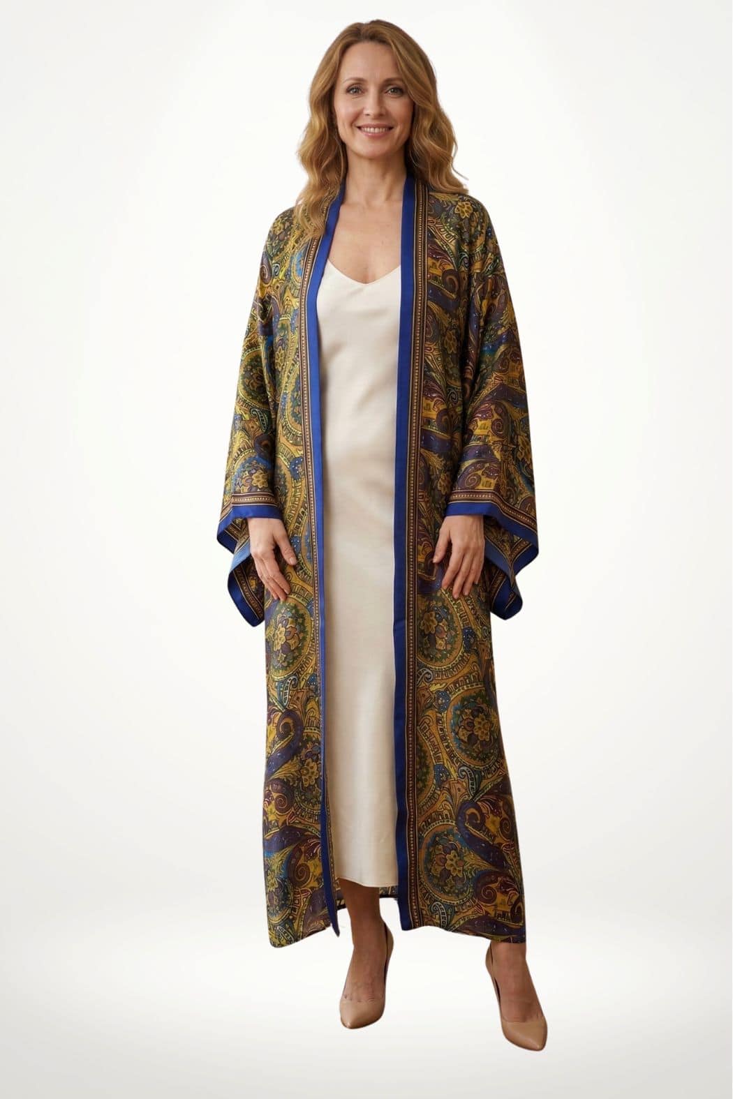 Femme souriante portant un kimono long aux motifs colorés, avec un fond blanc et des chaussures beiges